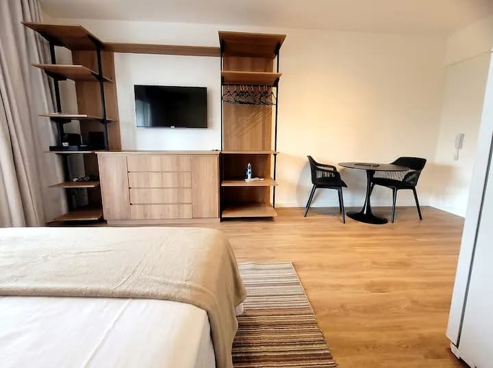 estante com TV, arara com cabides e mesa redonda